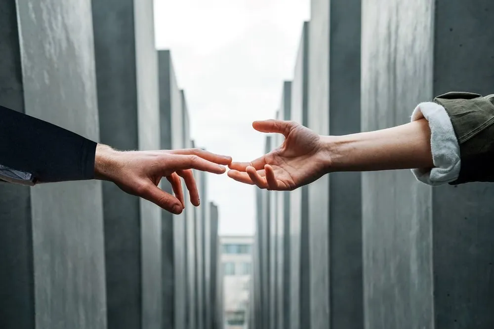 Two hands reaching towards each other between tall concrete pillars