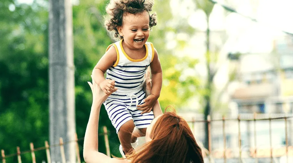 Laughing toddler lifted into the air by a woman outdoors