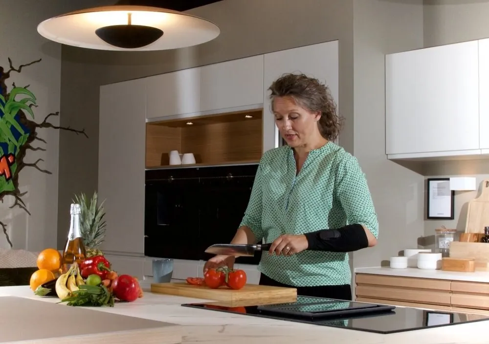 Woman slicing tomatoes in a kitchen, wearing a black sensor sleeve on her forearm