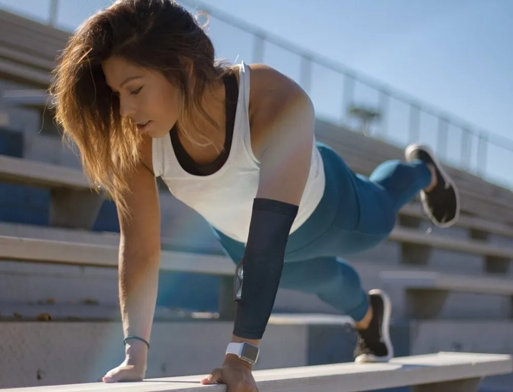 Woman holding a plank on stadium steps, wearing a black sensor sleeve on her forearm